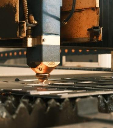 Ein Laser-Schneidkopf einer industriellen CNC-Laserschneidanlage bearbeitet eine Metallplatte.